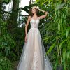 Braut in einem transparenten A-Linien-Brautkleid mit floralen Applikationen und Tüllrock, posierend in einem tropischen Gewächshaus.