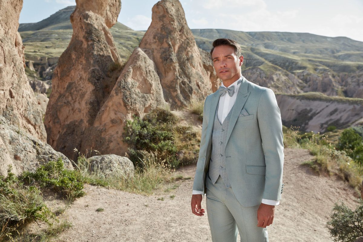 Hellgrüner Hochzeitsanzug für Bräutigam mit Weste und Einstecktuch vor Felslandschaft im Freien