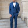 Eleganter dreiteiliger Bräutigamanzug in Königsblau mit Fliege und braunen Lederschuhen, getragen von einem stilvollen Herren auf Steintreppen.