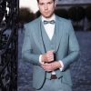 Stilvoller, hellgrauer Bräutigamanzug mit Weste und Fliege, getragen von einem eleganten Herren bei Dämmerlicht am schmiedeeisernen Tor.