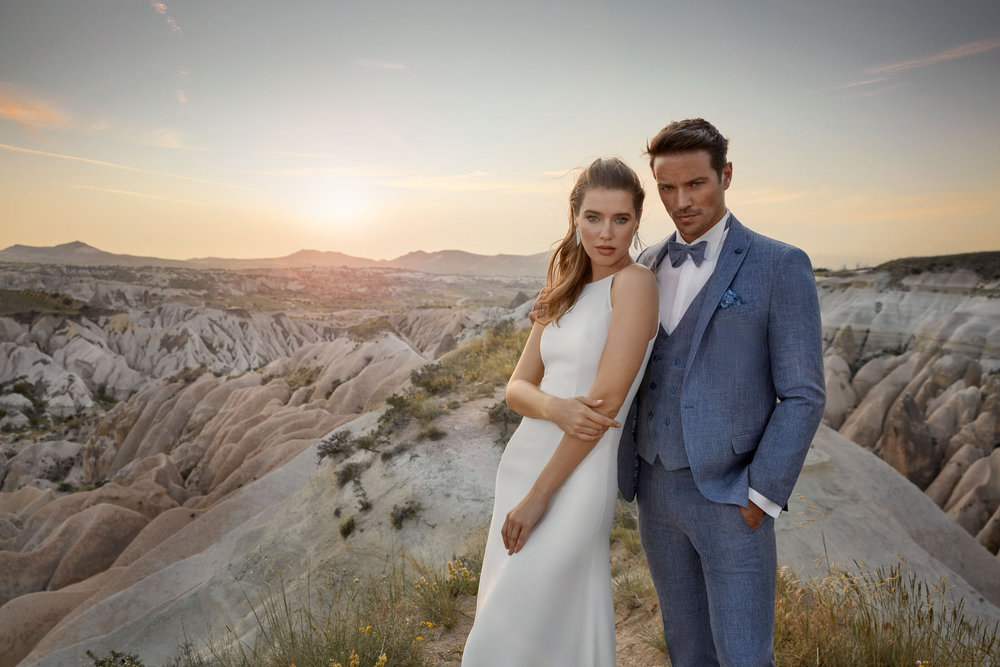Blauer Bräutigamanzug mit Weste und Fliege – eleganter Hochzeitsanzug in Kombination mit einem schlichten weißen Brautkleid in natürlicher Umgebung.