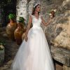 Prinzessinnen-Brautkleid mit Tüllrock, tiefem Tattoo-Rückenausschnitt und Knopfleiste, romantische Kulisse mit Blumenkranz.