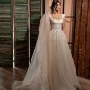 Romantisches, glitzerndes Brautkleid mit Schleppe, transparenter Corsage und Tüllärmeln in einem eleganten Innenraum, aufgenommen im Abendlicht.