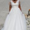Curvy Braut in romantischem Brautkleid mit Spitzenoberteil und ausgestelltem Tüllrock am Strand.